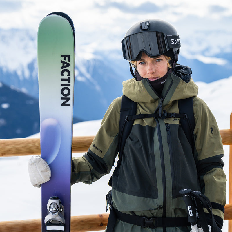 Skier with black helmet and dark green jacket holding green and blue ski.