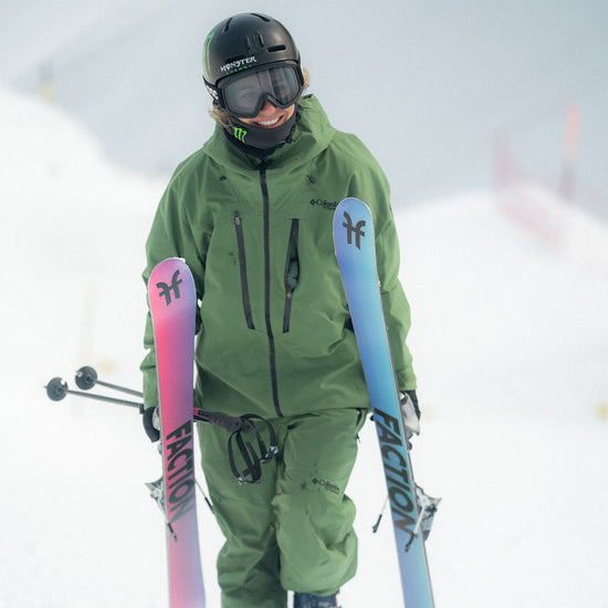 Sarah Hoefflin walking up a snow park showing the Faction Studio 0 skis colourful bases..