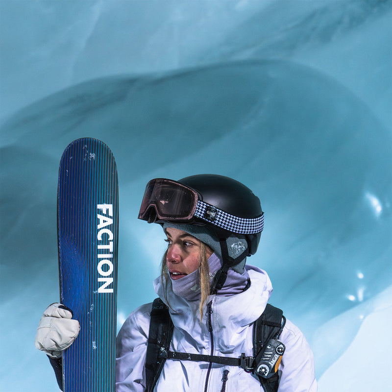 Skier with light purple jacket and black helmet holding a blue ski in an ice cave.