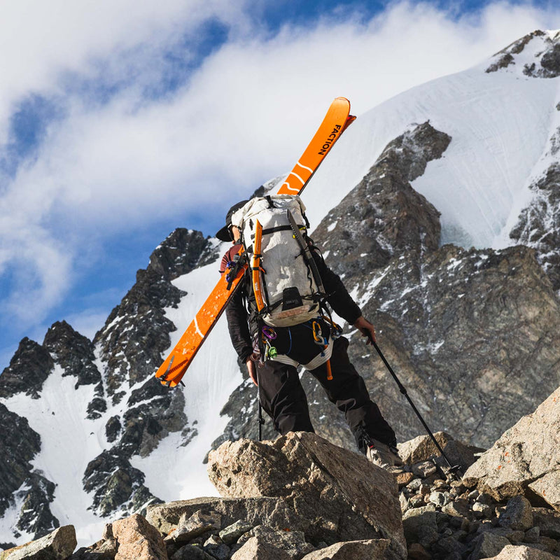 Person with Faction Agent 3 touring skis on their back climbing a rocky mountain peak