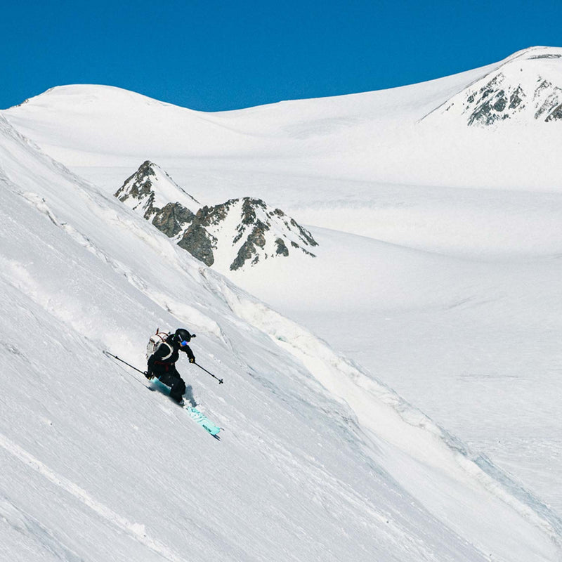 Skiier descending a snowy mountain with clear blue sky on Faction Agent 3 Skis