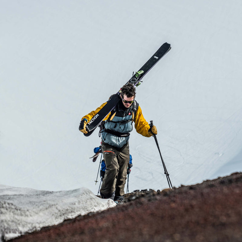 Person carrying skis over their shoulder on a snowy landscape