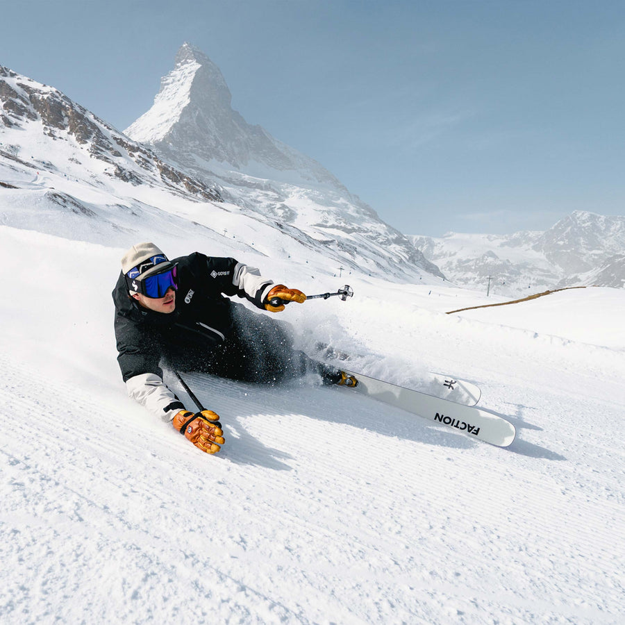 Skier carving on piste with the Faction Dancer 89 TI with a sunny mountain background