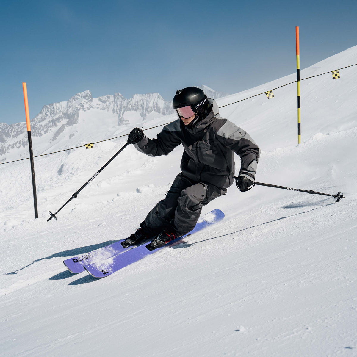 Skier in action with the purple Faction Dancer 99 on a snowy slope with mountains in the background