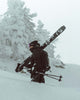 Person carrying skis and poles through a snowy landscape with trees.