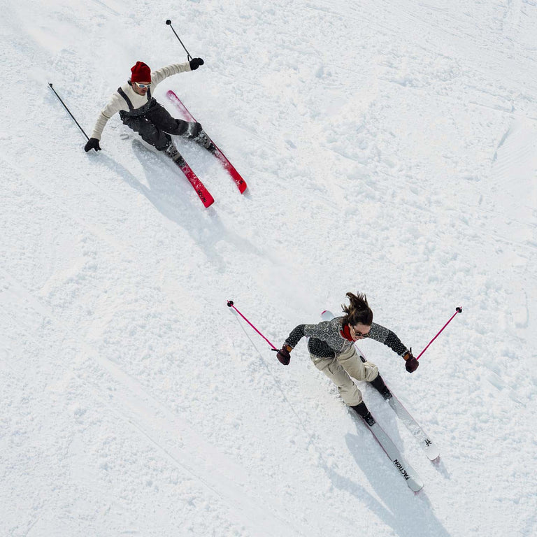 Two skiers skiing across a snowy landscape from an aerial perspective.