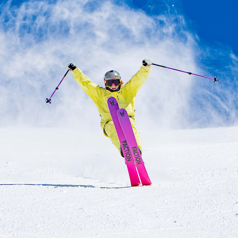Person skiing with a bright yellow jacket and pink skis against a blue sky.